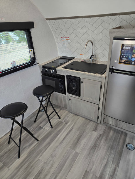 Modern RV rental galley featuring a compact kitchen with a sink, stovetop, microwave, fridge, and two bar stools.