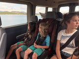 Three kids in an RV rental looking out at a large lake and distant hills on a scenic family road trip.