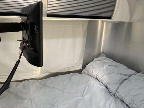 Cozy RV rental bedroom with a mounted TV, soft grey quilted bedding, and metallic walls. Ideal for comfortable travel.