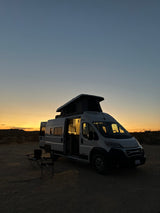 Enjoying a serene desert sunset from an RV rental pop-top camper van, chairs set for stargazing.