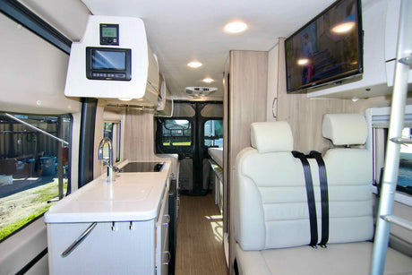 View inside a sleek rv rental: a compact kitchen, electronic controls, comfortable seating, and wall-mounted TV.
