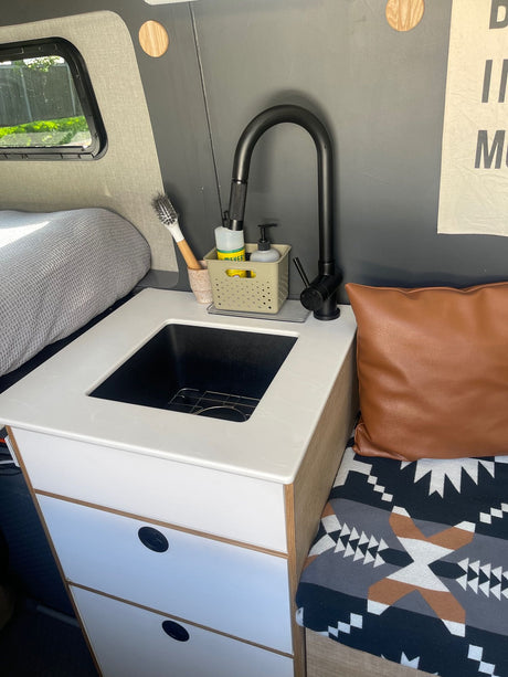 Inside a modern RV rental, featuring a functional kitchen sink, comfortable bed, and stylish seating area.