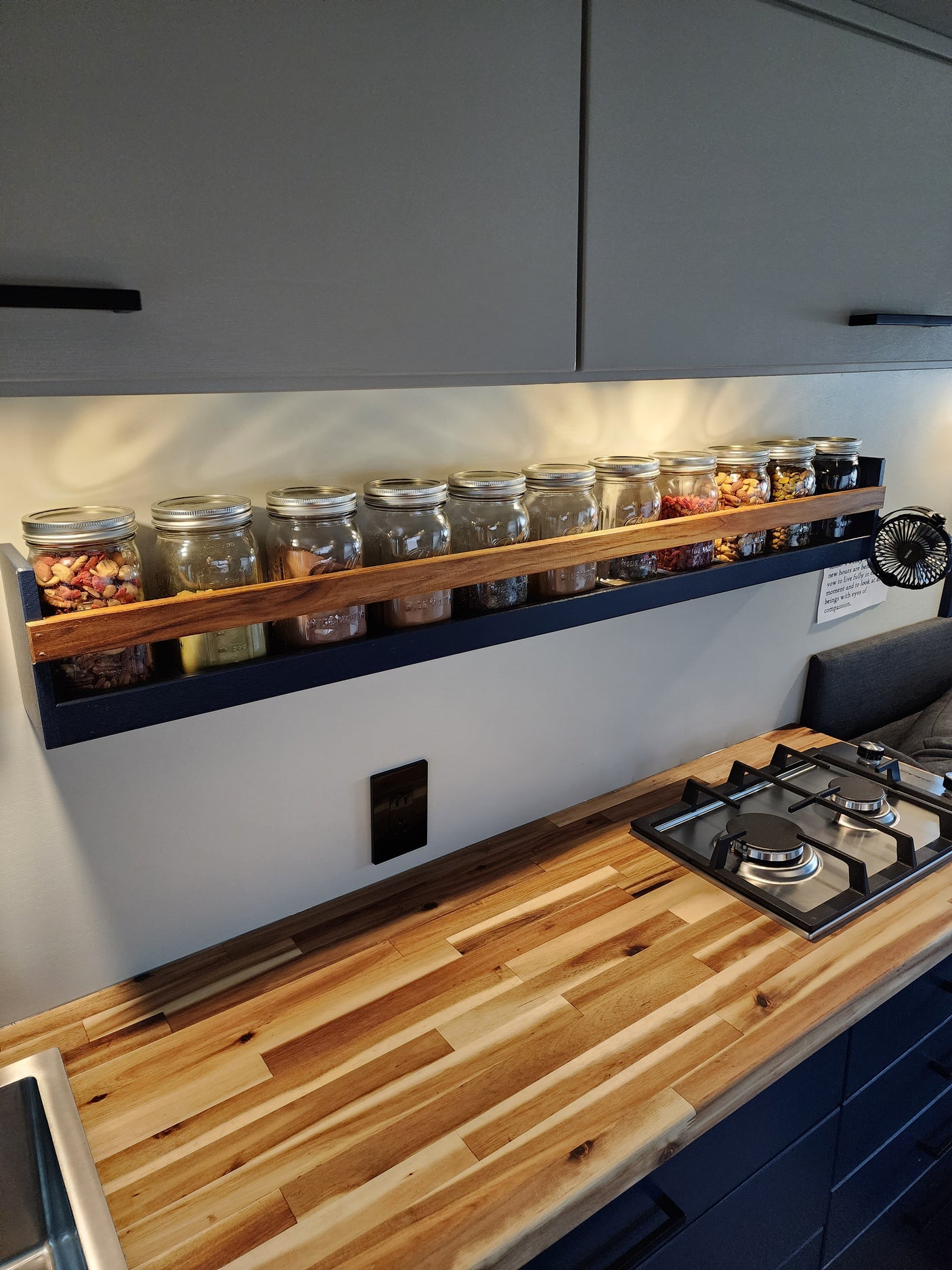 This RV rental kitchen maximizes space with a vertical spice rack displaying many clear jars, a gas stovetop, and wood countertop.