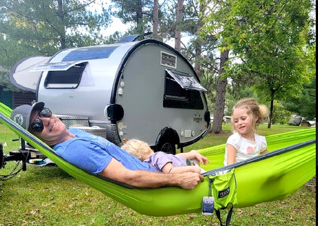 Dad and kids relax in a vibrant green hammock, enjoying outdoor family fun beside their rv rental.