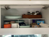 An organized RV rental kitchen cabinet, displaying stacked dishes, mugs, spices, and snacks on a shelf rack.
