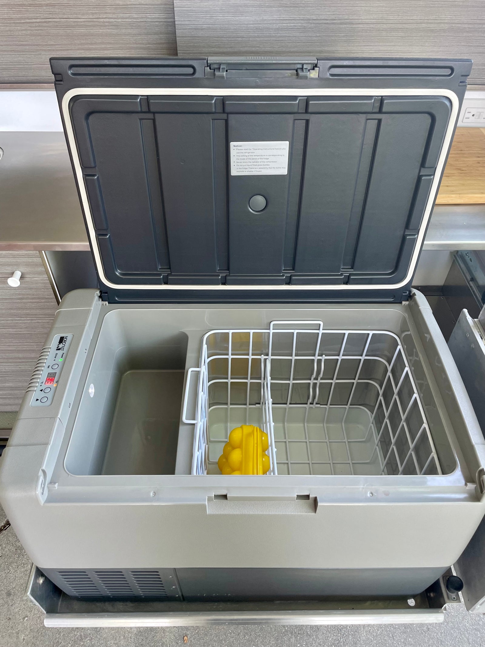 An open portable refrigerator, often found in an RV rental, showing its dual compartments, wire basket, and controls.