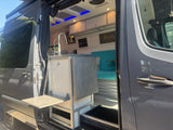 Step inside this grey RV rental! View of the custom interior featuring a modern kitchen with sink, cozy blue seating, and overhead cabinets.