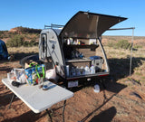 Outdoor kitchen of a Freesolo RV rental setup in the desert for camping. Table with groceries, water jugs, tent visible.