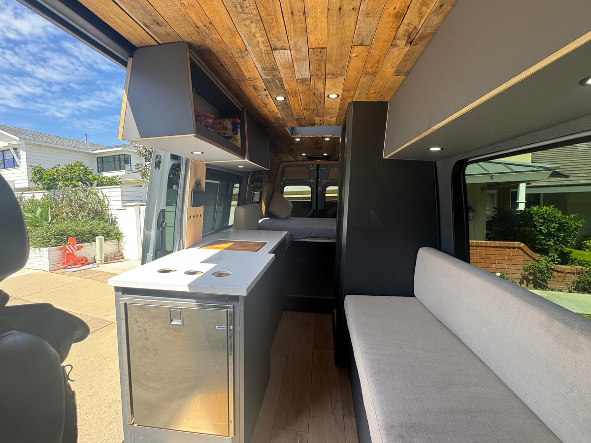 Stylish RV rental interior: a modern camper van featuring a kitchenette with fridge, seating area, bed, and custom wooden ceiling. — photo 6