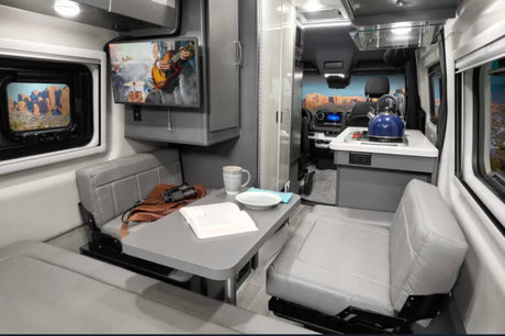 RV rental: The cozy, modern interior of a camper van with dining, kitchen, and wall-mounted TV.