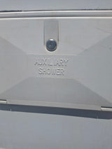 White auxiliary shower access panel on an RV rental, featuring a keyhole and "AUXILIARY SHOWER" text. For outdoor use.