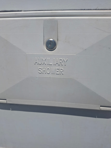 White auxiliary shower access panel on an RV rental, featuring a keyhole and "AUXILIARY SHOWER" text. For outdoor use.