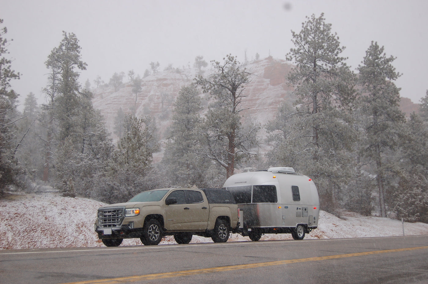 A truck towing a silver Airstream RV in a snowy mountain landscape. Consider an rv rental for winter escapes. — photo 3