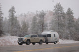 A truck towing a silver Airstream RV in a snowy mountain landscape. Consider an rv rental for winter escapes.