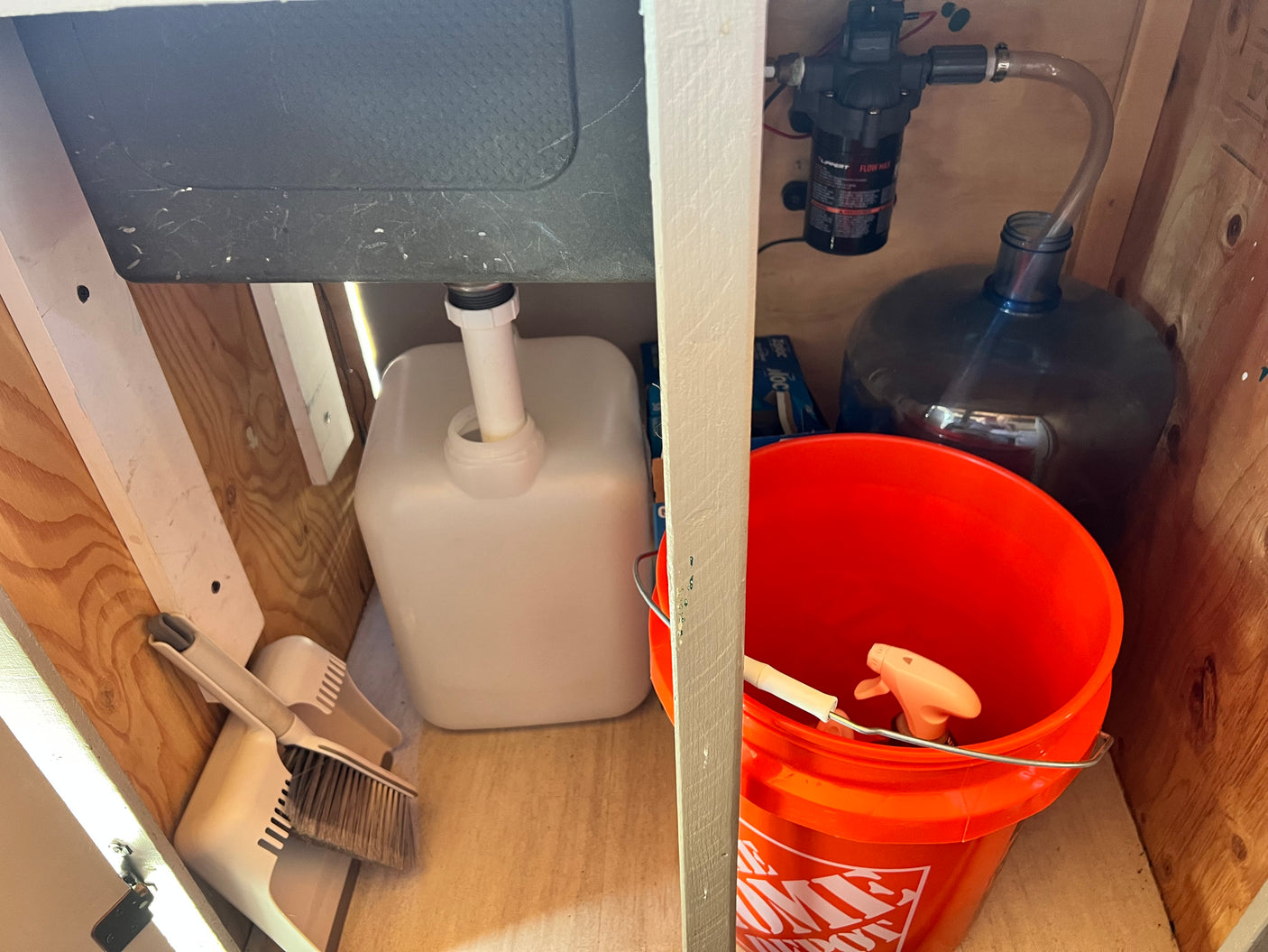 RV rental: Under-sink area with portable water pump, fresh water bottle, grey water tank, and cleaning supplies.