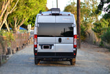 A silver Winnebago Sol camper van, available for rv rental, seen from the rear on a sunlit gravel road.