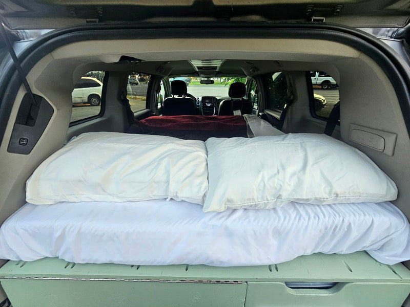 Inside an RV rental: a transformed minivan features a comfy bed with white pillows and a custom storage platform. — photo 5