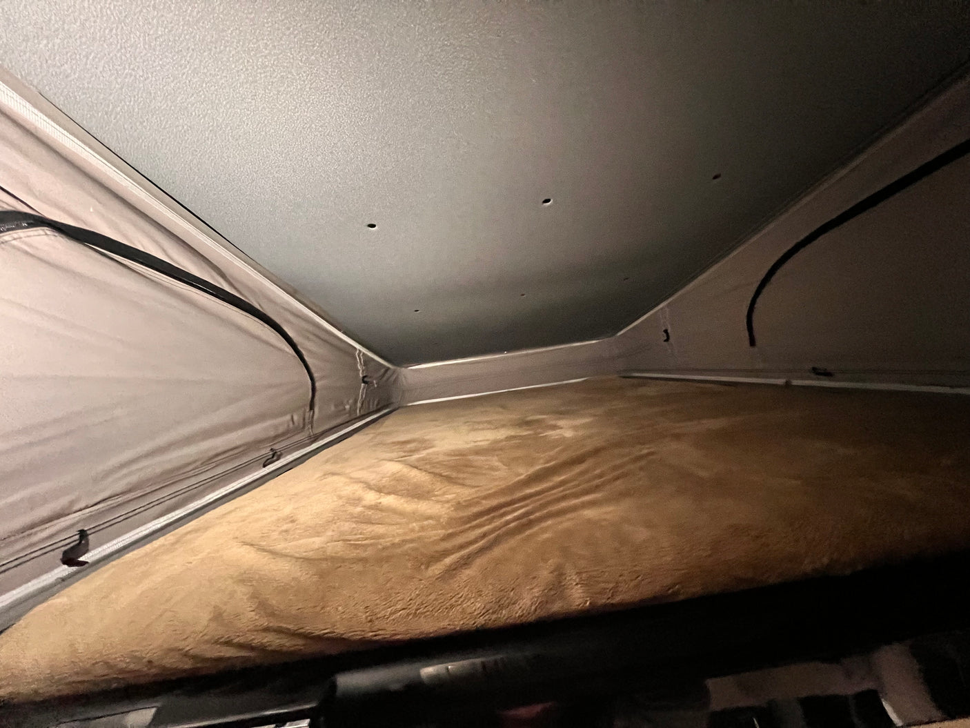 Cozy pop-top sleeping area of an RV rental with a soft brown blanket, fabric walls, and a grey ceiling, ready for rest.