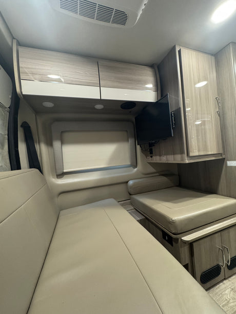 Step inside this RV rental featuring comfortable beige benches, wood-grain overhead cabinets, and a wall-mounted TV for your trip.