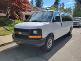 White Chevrolet van with a roof rack, great for an RV rental. Parked on a sunny street with houses and trees.