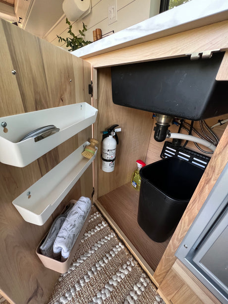 RV rental kitchen sink cabinet: smart storage for cleaning supplies, trash, and a fire extinguisher.