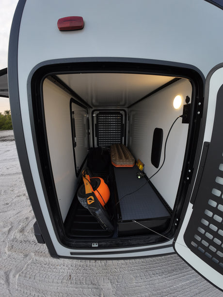 RV rental's illuminated side storage, packed with adventure gear: Onewheel, traction boards, and a power outlet.