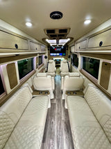 Luxury RV rental interior featuring cream quilted leather seats, wood-look flooring, overhead storage, and a large entertainment screen.