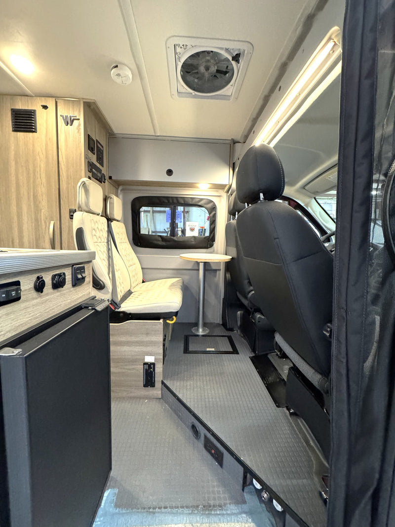 This RV rental interior shows swiveling front seats, a dining table, kitchenette, and overhead storage, perfect for a road trip. — photo 10