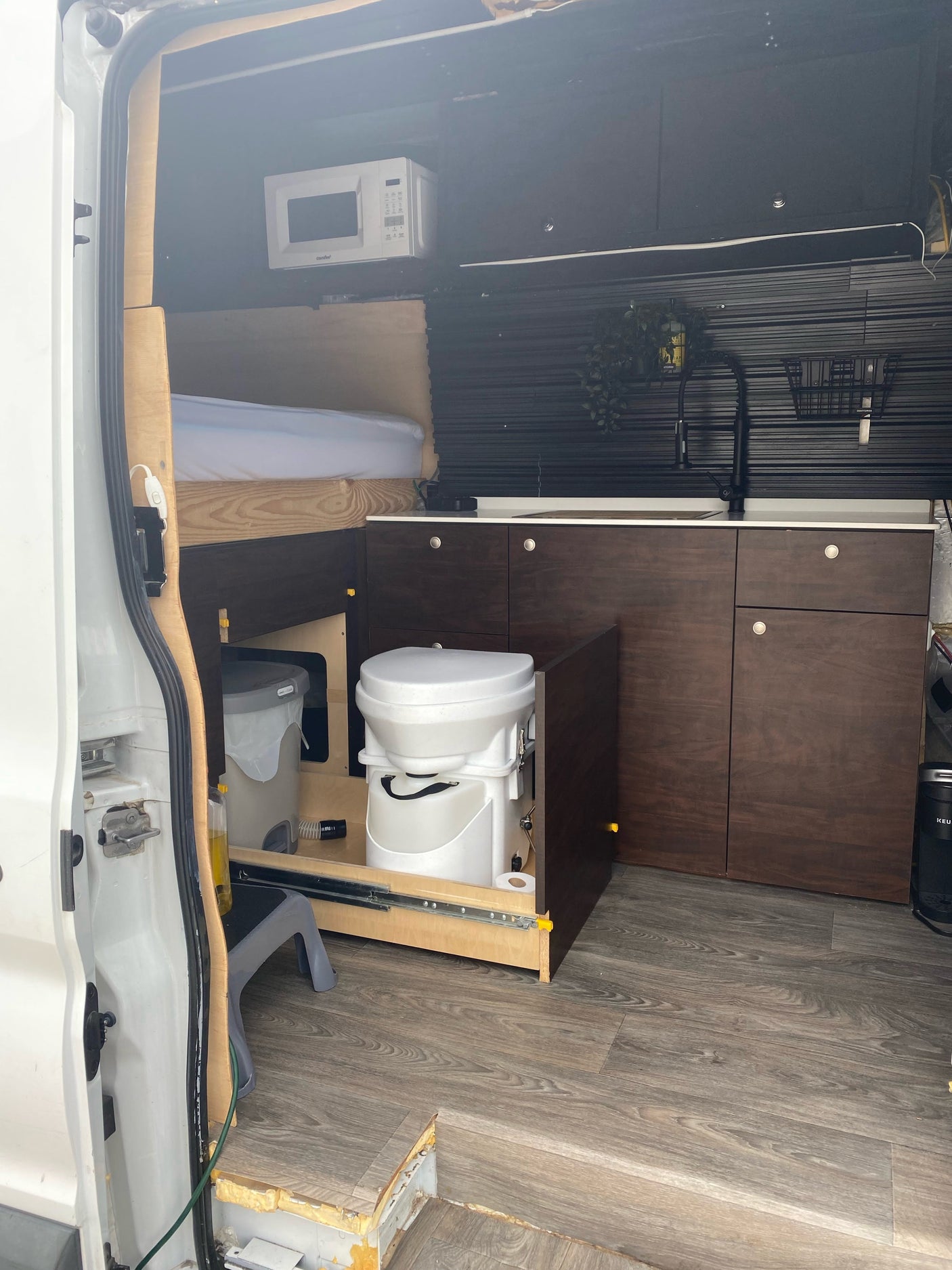 Inside this RV rental van, a full conversion with a bed, kitchenette, microwave, and clever pull-out toilet system.
