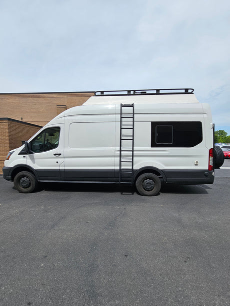 White Ford Transit RV rental camper van, featuring a roof rack, side ladder, and spare tire on the back.
