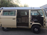 RV rental: Beige VW camper van with open side and front doors, showcasing its interior and pop-top roof design.
