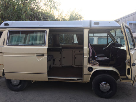 RV rental: Beige VW camper van with open side and front doors, showcasing its interior and pop-top roof design.