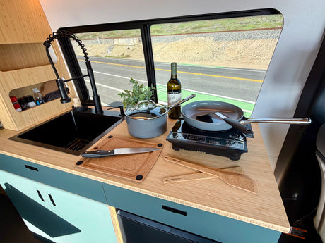 Well-equipped RV rental kitchen featuring a sink, induction cooktop, and cookware, ideal for cooking while traveling.