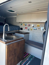 Explore this RV rental's clever interior: high bed, sink kitchen, and bench. Ideal for mobile living & travel adventures.