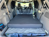 RV rental alternative: Minivan interior transformed for car camping. Features a comfortable bed, under-bed storage, and privacy curtains.