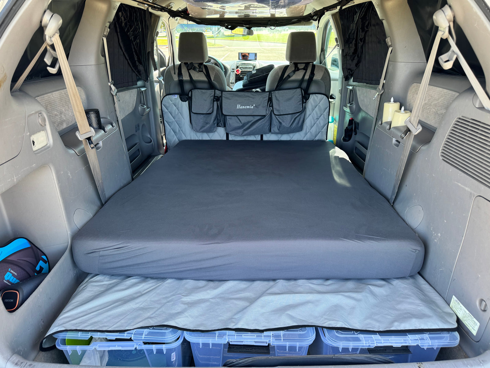 RV rental alternative: Minivan interior transformed for car camping. Features a comfortable bed, under-bed storage, and privacy curtains.
