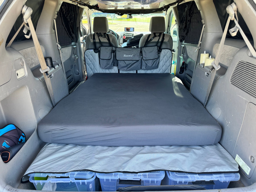 RV rental alternative: Minivan interior transformed for car camping. Features a comfortable bed, under-bed storage, and privacy curtains.