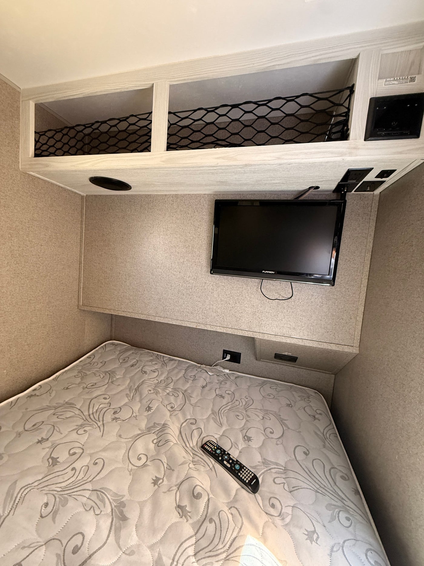 This compact RV rental bedroom features a TV, overhead storage nets, and a cozy mattress with a remote. — photo 5