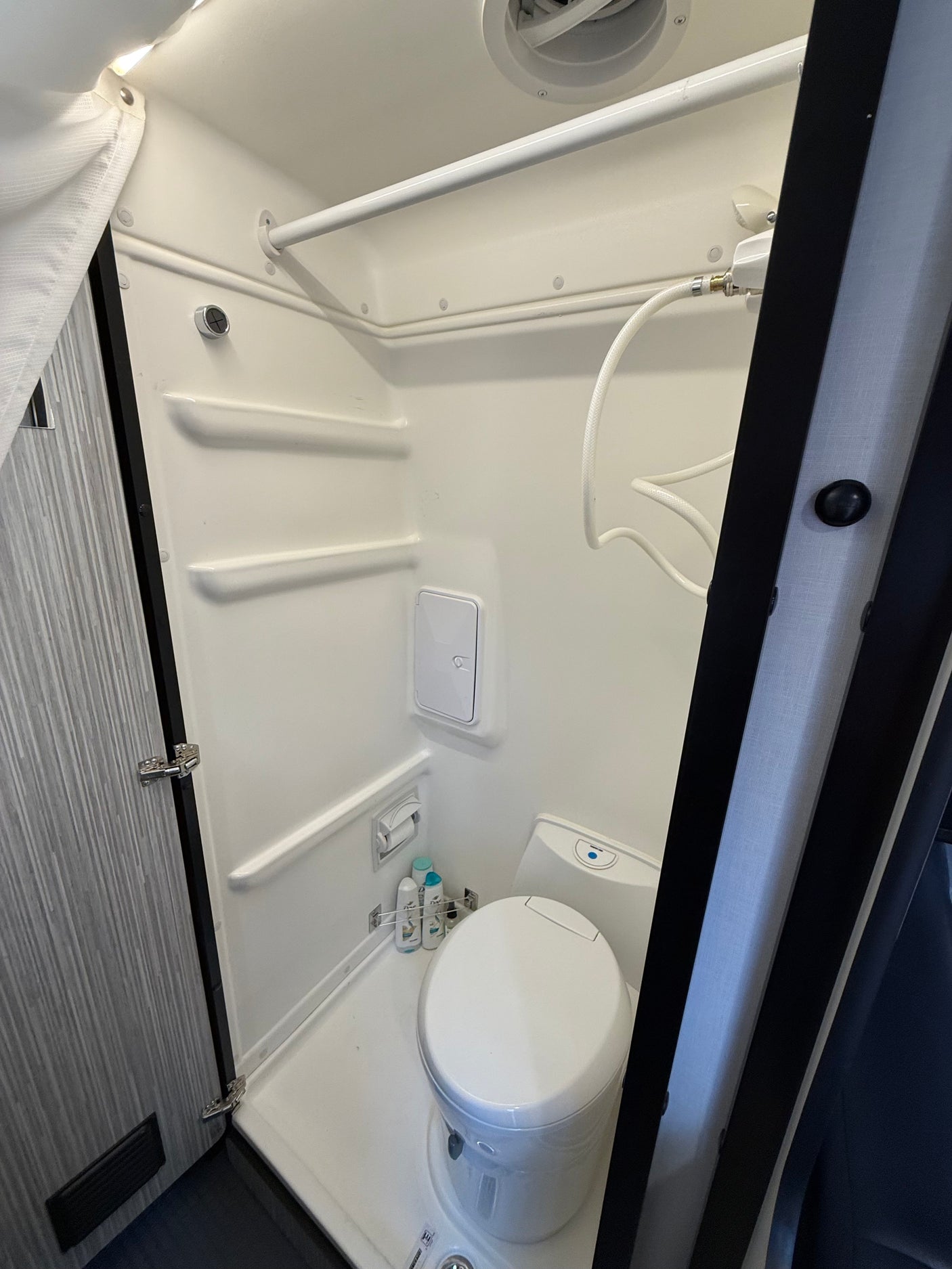 This RV rental features a compact wet bath with a toilet, shower, and built-in shelving.