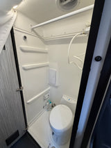 This RV rental features a compact wet bath with a toilet, shower, and built-in shelving.