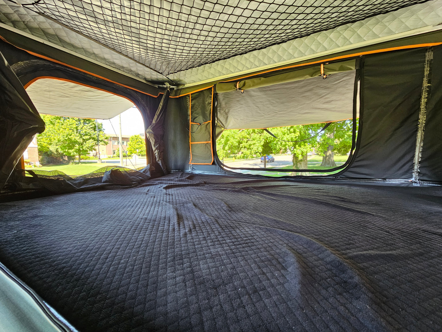 Cozy interior of an RV rental rooftop tent, featuring a quilted sleeping area and open windows with outdoor views.