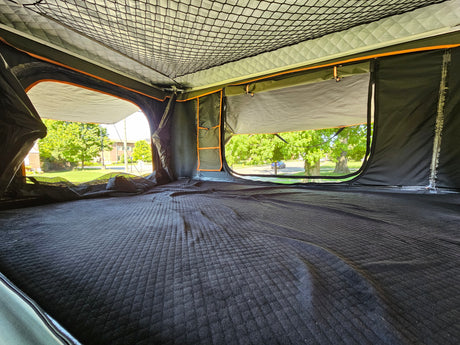 Cozy interior of an RV rental rooftop tent, featuring a quilted sleeping area and open windows with outdoor views.
