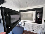An open, compact microwave showing its interior, built into a small, functional kitchen within an RV rental.
