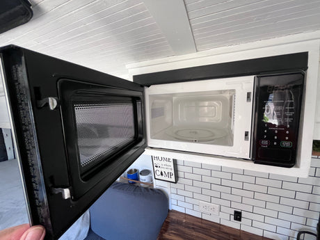 An open, compact microwave showing its interior, built into a small, functional kitchen within an RV rental.