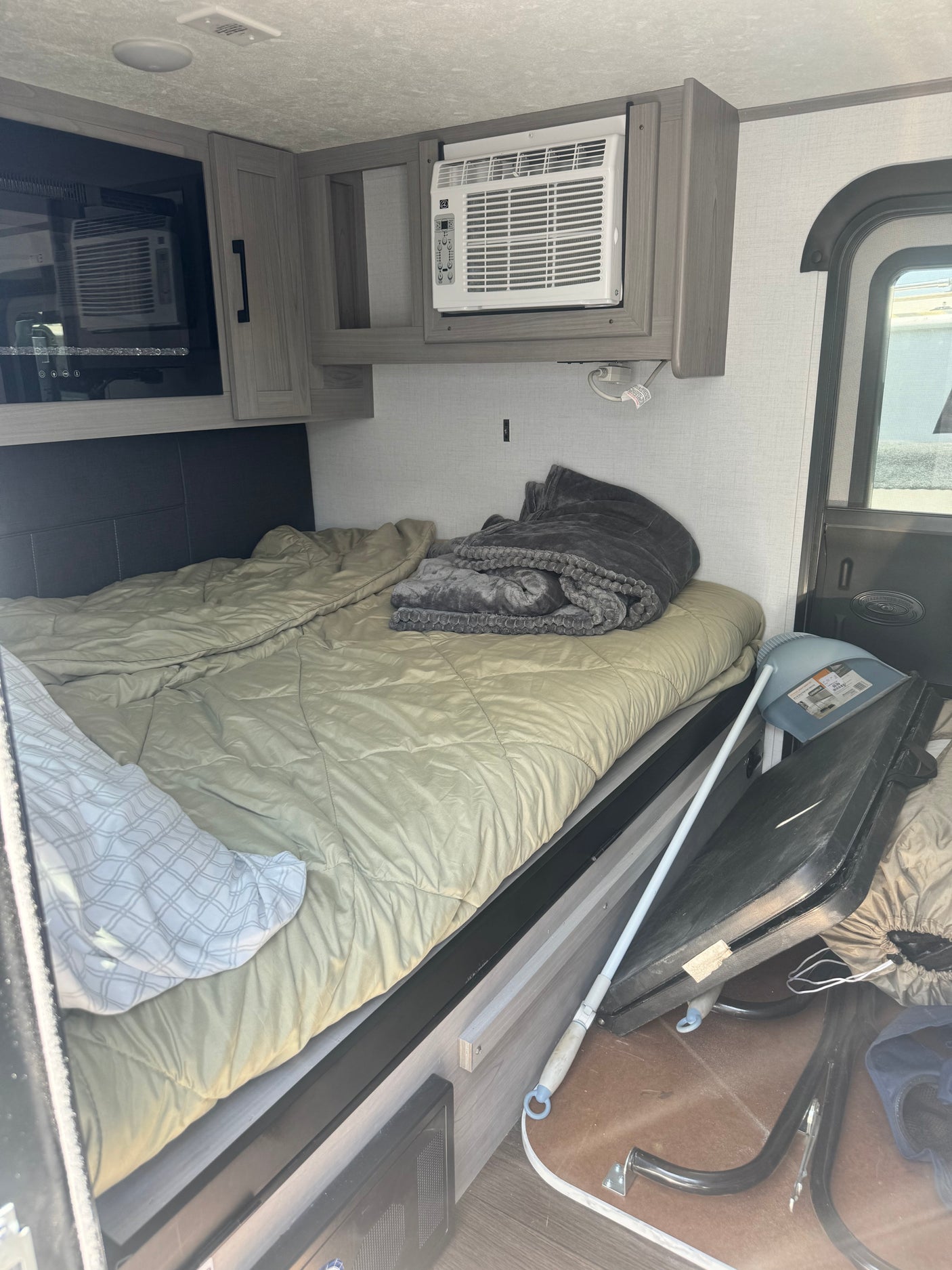 Inside an RV rental: a comfortable bed with AC and microwave overhead, plus storage. Ready for travel.
