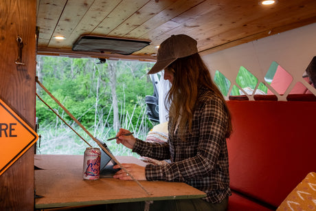 Working remotely in an RV rental: A woman uses a tablet in a cozy van, enjoying forest views outside.