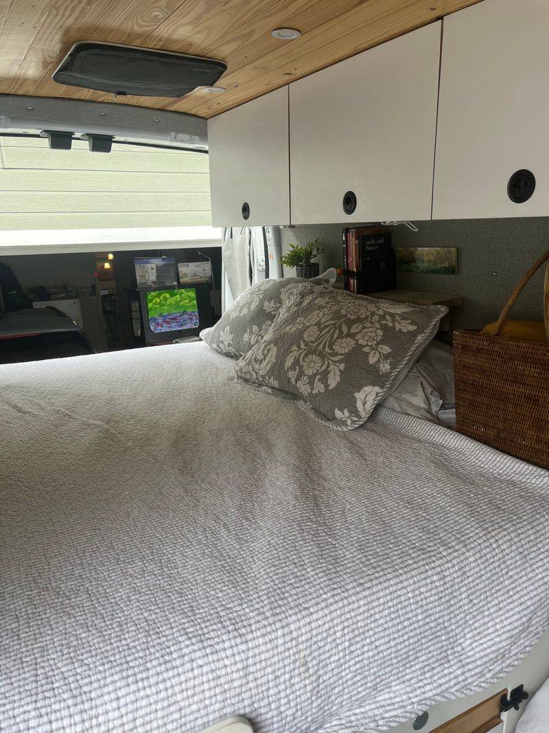 Inside a comfy RV rental: bed with grey bedding, wood ceiling, overhead cabinets, and a view outside the window. — photo 9