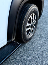 White RV rental van: tire, multi-spoke wheel, and running board on asphalt, showing vehicle detail.