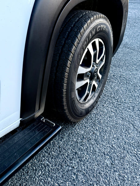 White RV rental van: tire, multi-spoke wheel, and running board on asphalt, showing vehicle detail.