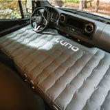 A grey LUNA inflatable mattress perfectly fits an RV rental van's front seats & dashboard, creating a cozy sleeping area for travelers.